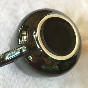 May include: Black ceramic mug with a white rim and a glossy finish. The mug has a handle and is empty.