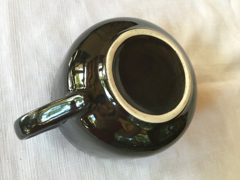 May include: Black ceramic mug with a white rim and a glossy finish. The mug has a handle and is empty.