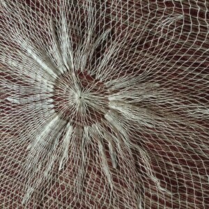 May include: A white net with a circular pattern in the center. The net is made of thin, white string and has a delicate, lacy appearance.