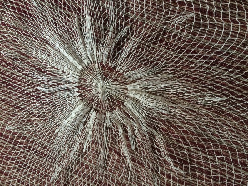 May include: A white net with a circular pattern in the center. The net is made of thin, white string and has a delicate, lacy appearance.