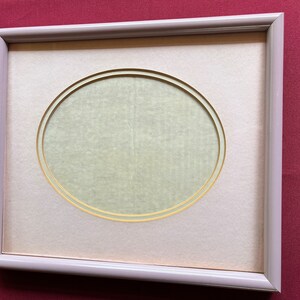 May include: A light gray picture frame with a white mat and a gold oval cutout. The oval cutout is empty.