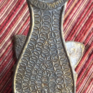 May include: A vintage brass bottle opener with a decorative design. The opener features a circular handle and a patterned body with a shield-shaped end. The text "SEIFERT BRASS" is visible on the bottom.