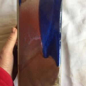 Op de afbeelding: Een rechthoekige keramische tegel met een bruine, blauwe en witte glazuur. De glazuur heeft een craquel&eacute;-effect.