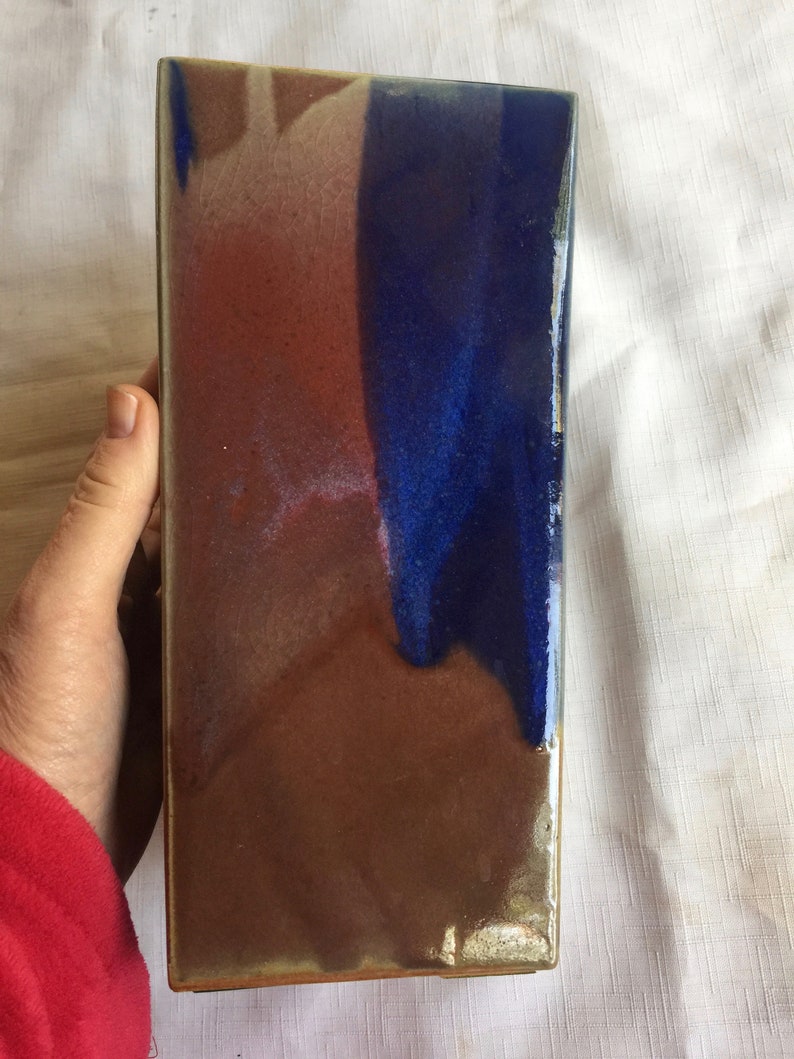 Op de afbeelding: Een rechthoekige keramische tegel met een bruine, blauwe en witte glazuur. De glazuur heeft een craquel&eacute;-effect.