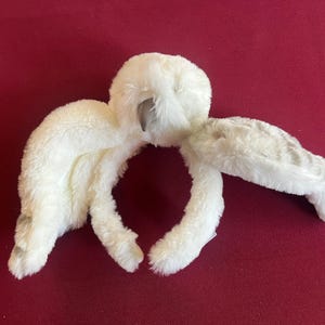 Puede incluir: Un peluche de búho blanco con detalles grises sobre un fondo rojo. El búho tiene una cabeza redonda, ojos grandes y alas extendidas. El juguete de peluche está hecho de un material suave.