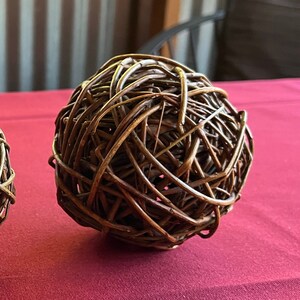 May include: A brown woven sphere made of thin twigs, resembling a ball of yarn. The sphere is sitting on a red surface.