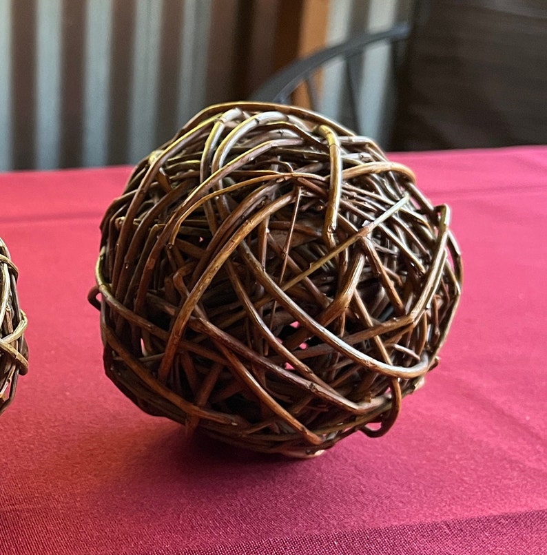 May include: A brown woven sphere made of thin twigs, resembling a ball of yarn. The sphere is sitting on a red surface.