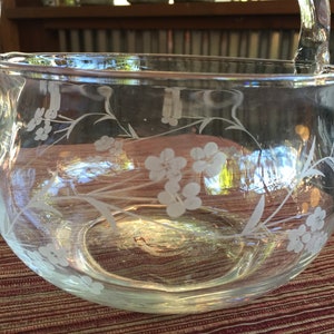 May include: A clear glass bowl with a floral design etched into the side. The bowl has a handle and is perfect for serving snacks or fruit.