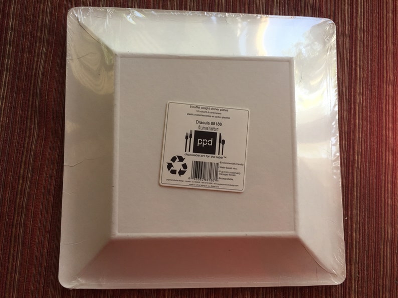 May include: A package of 8 white, square, disposable dinner plates. The package is labeled "Dracula 801186" and "Plated Kitchen" with a logo that says "ppd". The plates are made from plant-based materials and are compostable.