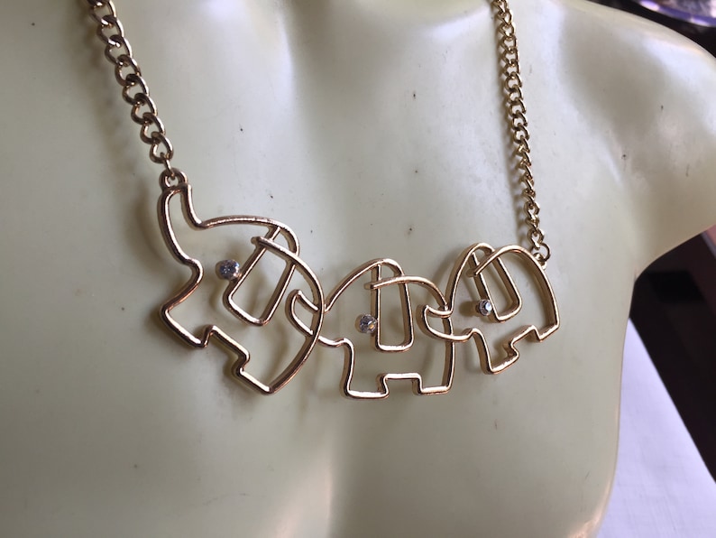May include: Gold necklace with three connected elephant charms, each with a small clear rhinestone in the center.