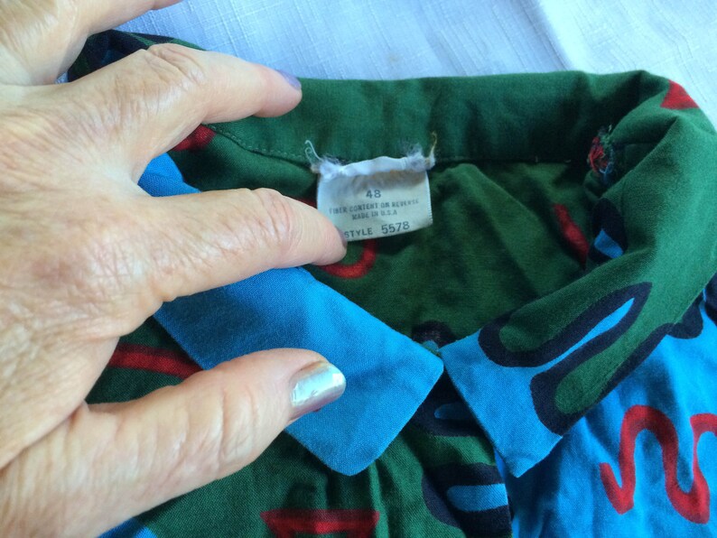 K&ouml;nnte beinhalten: Ein gr&uuml;n-blau-rot-schwarz gemustertes Hemd mit blauem Kragen. Das Hemd hat ein Etikett mit der Aufschrift "48" und "Style 5578".