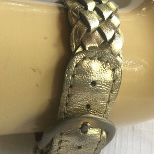 May include: A gold-colored leather watch band with a braided design and a silver buckle.