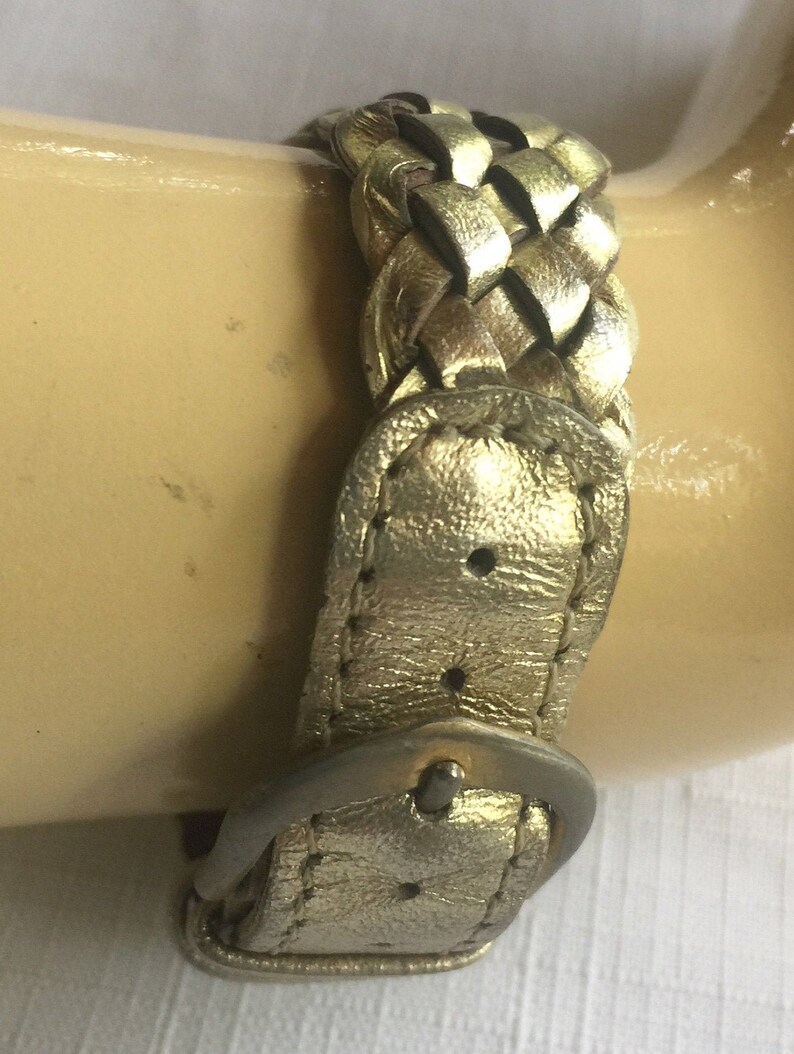 May include: A gold-colored leather watch band with a braided design and a silver buckle.