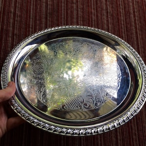 May include: A silver serving tray with a decorative embossed design. The tray has a raised rim and a smooth, reflective surface.