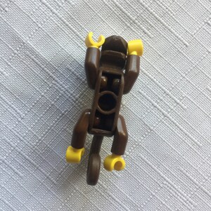 May include: A brown Lego monkey figure with yellow hands and feet. The monkey is in a sitting position with its arms raised above its head.