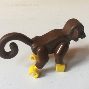 May include: A brown plastic monkey toy with a curled tail and yellow feet. The monkey is in a crouching position.