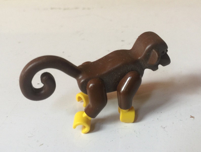 May include: A brown plastic monkey toy with a curled tail and yellow feet. The monkey is in a crouching position.