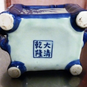 Peut inclure: Un pot en c&eacute;ramique bleu et blanc avec quatre pieds et une base carr&eacute;e. Le pot est d&eacute;cor&eacute; de branches et de feuilles de bambou. Le fond du pot porte un tampon carr&eacute; avec le texte "敬大 曜清" en caract&egrave;res chinois.