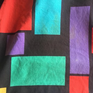 K&ouml;nnte beinhalten: Ein schwarzer Stoff mit einem geometrischen Muster aus roten, violetten, t&uuml;rkisfarbenen und gr&uuml;nen Quadraten.