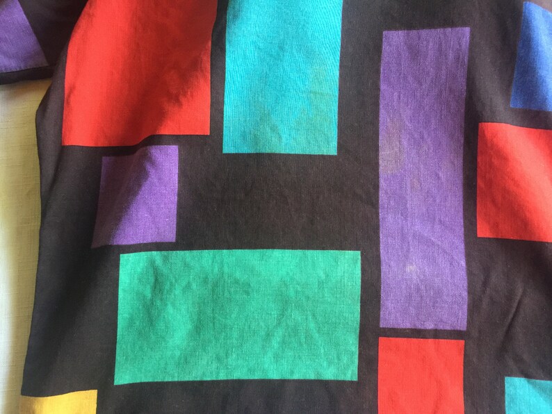 K&ouml;nnte beinhalten: Ein schwarzer Stoff mit einem geometrischen Muster aus roten, violetten, t&uuml;rkisfarbenen und gr&uuml;nen Quadraten.