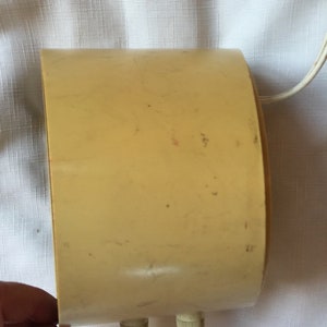May include: A cream-colored vintage alarm clock with two knobs on the bottom. The clock has a rounded shape and a cord attached to the back.