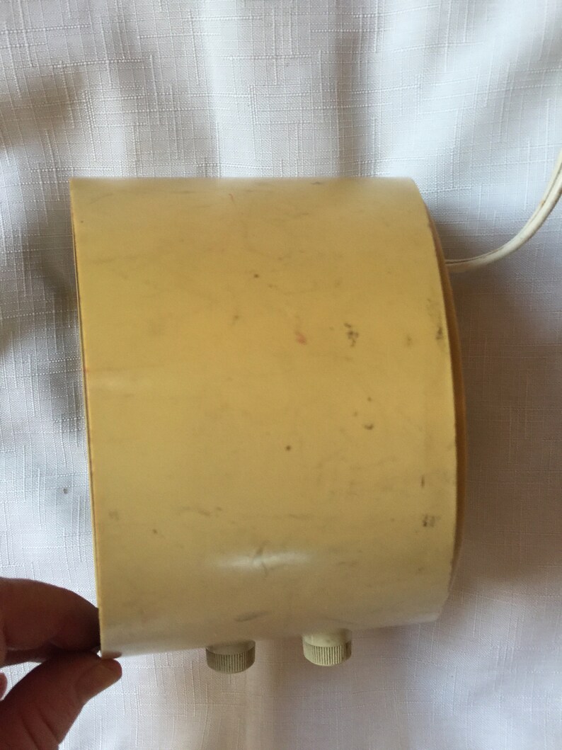 May include: A cream-colored vintage alarm clock with two knobs on the bottom. The clock has a rounded shape and a cord attached to the back.