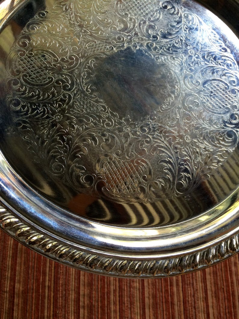 May include: A silver serving tray with an ornate, embossed design. The tray has a raised rim and a smooth, reflective surface.