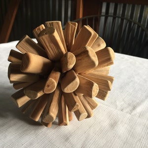 May include: A wooden sphere made of many small, natural wood pieces. The pieces are arranged in a radial pattern, creating a unique and organic texture.