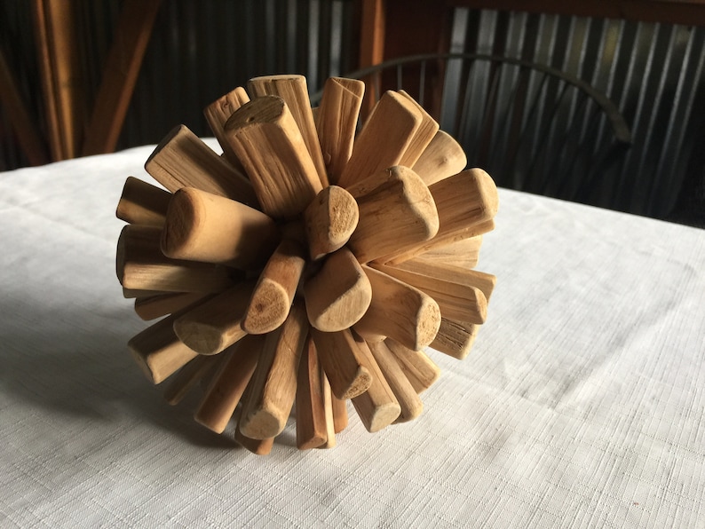 May include: A wooden sphere made of many small, natural wood pieces. The pieces are arranged in a radial pattern, creating a unique and organic texture.