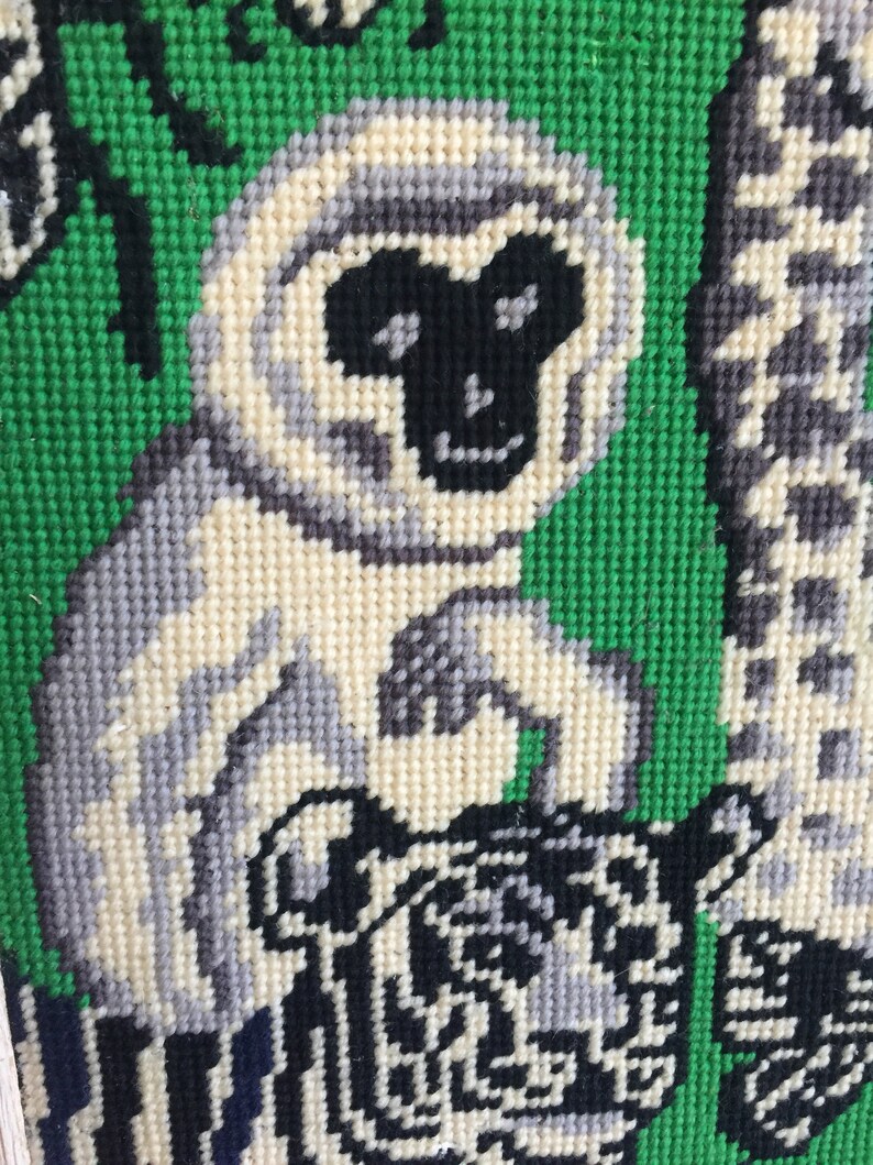 May include: A close-up of a needlepoint tapestry featuring a white monkey with a black face and a black and white tiger. The background is green.