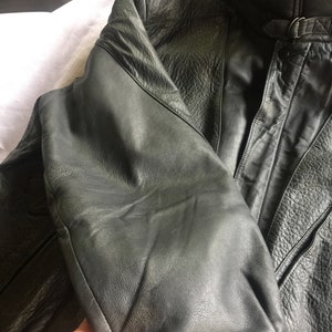 Pu&ograve; includere: Una giacca di pelle grigio scuro con chiusura a zip e un dettaglio con fibbia sul collo.