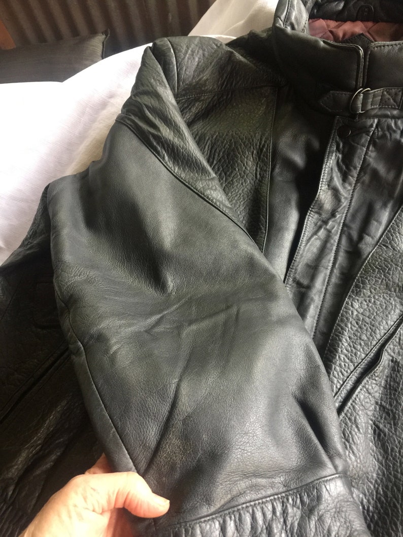 Pu&ograve; includere: Una giacca di pelle grigio scuro con chiusura a zip e un dettaglio con fibbia sul collo.