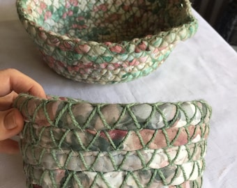 Puede incluir: Dos cestas tejidas hechas con recortes de tela. La cesta más grande tiene un asa y es verde, rosa y blanca. La cesta más pequeña es verde y rosa con un estampado floral.
