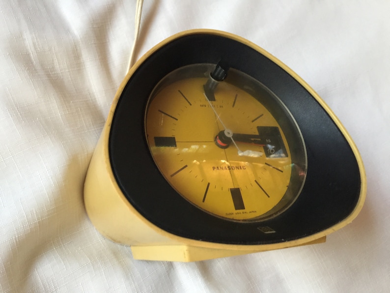 May include: A yellow and black vintage Panasonic alarm clock with a round face and a black bezel. The clock has a white background with black hour and minute hands and a red second hand. The clock is set to 10:51.