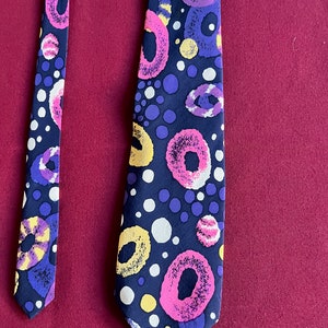 May include: A black silk tie with a colorful abstract pattern of pink, purple, yellow, and white circles and dots.