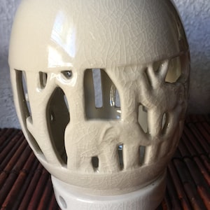 May include: A white ceramic candle holder with a crackled glaze and a design of elephants cut out of the sides. The holder has a round base.