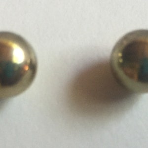 Könnte beinhalten: Ein Paar goldfarbene Kugelohrstecker.