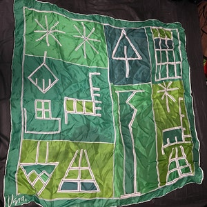 May include: A green silk scarf with a geometric pattern of white lines. The pattern includes stars, trees, and other abstract shapes.