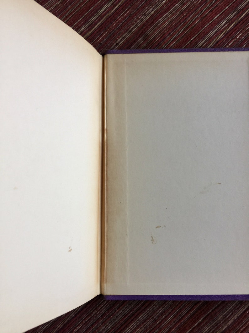 May include: An open book with a purple cover and white pages. The pages are slightly yellowed with age and there are a few brown spots on the right page.