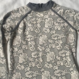 May include: A long-sleeved, grey and white floral patterned shirt with a mock neck and grey trim around the neckline and sleeves.
