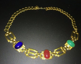 Puede incluir: Un collar de cadena de oro con tres piedras preciosas de forma ovalada. Las piedras preciosas son azules, rojas y verdes.