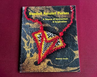 May include: A book titled "Beaded Amulet Purses" with a beaded amulet design on the cover. The amulet is red, yellow, black, and white. The book also includes the text "A Source of Instruction & Inspiration" and the author's name, Nicolette Stessin.
