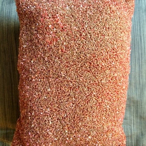 Puede incluir: Una almohada de color coral con una superficie texturizada y con lentejuelas.