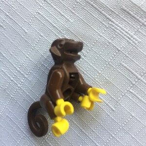 May include: A brown plastic monkey figurine with yellow hands and a curled tail. The monkey is sitting with its legs bent and its arms outstretched.