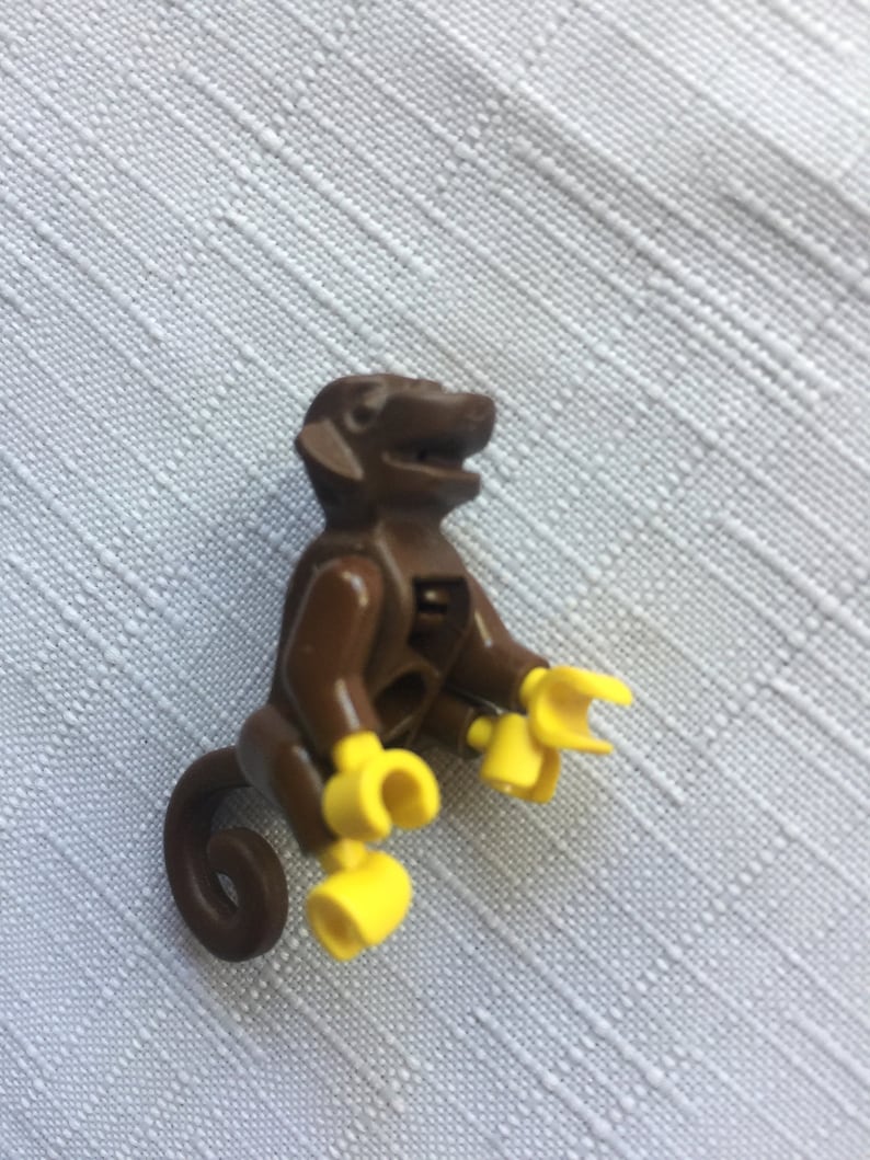 May include: A brown plastic monkey figurine with yellow hands and a curled tail. The monkey is sitting with its legs bent and its arms outstretched.