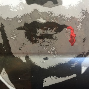 May include: A close-up of a person's face with a black and white filter. The person's lips are painted black and there is a red splatter of paint on their cheek.