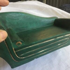 May include: A small, green wooden sofa with gold trim. The sofa is made of wood and has a simple, elegant design.