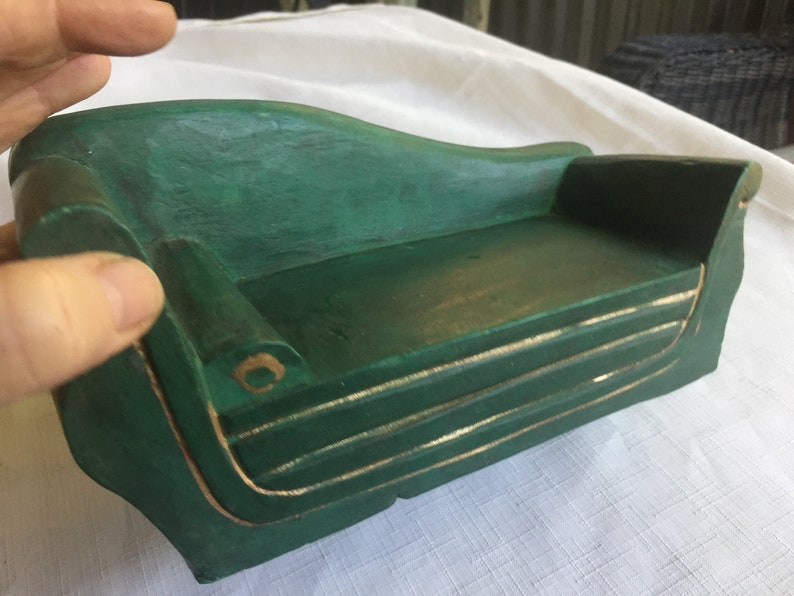 May include: A small, green wooden sofa with gold trim. The sofa is made of wood and has a simple, elegant design.