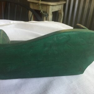 May include: A small, green wooden couch for a dollhouse. The couch is made of wood and has a simple design.