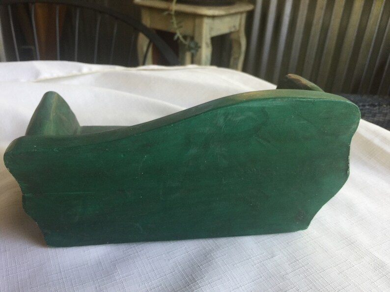 May include: A small, green wooden couch for a dollhouse. The couch is made of wood and has a simple design.